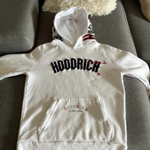 Vit hoodie från Hoodrich med tryck - Säljer en vit hoodie från Hoodrich i storlek S. Tröjan har svart och rött broderat tryck framtill, stor magficka och coolt tryck på ryggen. Huvan har unika detaljer i svart och rött. Perfekt för dig som gillar streetwear och vill sticka ut. Original pris: 950 kr fast jag säljer för 750 kr istället (kan gå ner till 700)