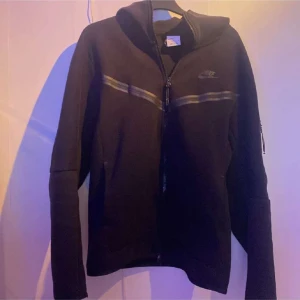 Svart Nike tech - Tja säljer nu min nike tech då den har blivit för liten, den är sparsamt använt fast är ett litet hål nere vid dragkedjan men det är inget som syns när man bär den
