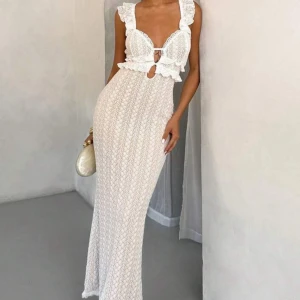 Vit lång spetsklänning med volang - Supersnygg långklänning i vit spets med volangdetaljer och djup v-ringning. Klänningen har ärmlös design, markerad midja och en liten cut-out framtill. Perfekt för dig som vill sticka ut med en romantisk och trendig look. Aldrig använd köpt för 359kr säljer för 200kr