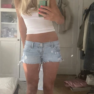 Ljusblå jeansshorts från Hollister - Snygga ljusblå jeansshorts från Hollister med låg midja och slitna detaljer. Råa, fransiga kanter och klassisk femficksmodell. Perfekta för sommaren och ger en avslappnad vibe. Ikonisk Hollister-logga på fickan och bak. Superbekväma och lätta att matcha. Midjemått:38cm, längden på shortsen är ca 25 cm