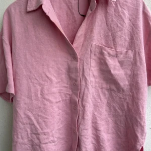 Rosa kortärmad skjorta från Stradivarius - Säljer en rosa skjorta från Stradivarius i storlek L. Skjortan har korta ärmar, klassisk krage, knäppning framtill och en bröstficka. Materialet är linne vilket ger en skön och luftig känsla. Perfekt för dig som gillar en avslappnad och trendig stil.