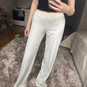 Vita kostymbyxor från Mango, storlek S - Snygga vita kostymbyxor från Mango med hög midja och raka, vida ben. Byxorna har pressveck framtill och dragkedja i sidan för en clean look. Perfekta att styla med crop top eller oversized skjorta för en fräsch vibe. Smutsiga vid fållen men märks inte vid användning (får ej bort) 