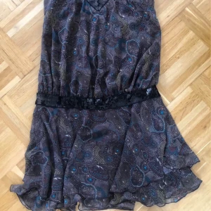 kortklänning från Repeat  - Kortklänning med coolt abstrakt mönster i brunt, blått och beige. Klänningen har breda axelband och v-ringning med svarta paljettdetaljer, samt markerad midja med paljettbälte. Luftigt material och flowig kjol ger en avslappnad vibe.