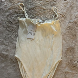 Vit body - Supersöt vit ribbad body från Zara med smala axelband och volangkant upptill. Har aldrig fått användning för det. Är som en S💕 Aldrig använd med lappen kvar