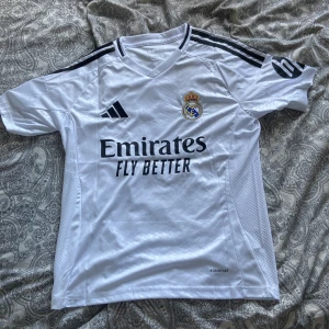 Real Madrid Mbappé 9 tröja - Säljer en vit Real Madrid fotbollströja från Adidas med Mbappé och nummer 9 på ryggen.  Champions League-märke på ärmen. Knappt använd. Priset är inte ristat i sten, men minst 300kr.