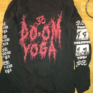 Svart långärmad Doom Yoga tröja - Svart långärmad tröja med stora röda och vita tryck fram och bak. Texten 'Doom Yoga' i metalstil och grafiska yogaposer på ryggen. Ärmarna har tryck med text och yogamotiv. Perfekt för dig som gillar alternativ stil och yoga.