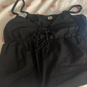 Svart linnetopp med snörning  - Svart linnetopp från Hm med smala axelband och snygg snörning framtill. Toppen har en lätt v-ringning och är tillverkad i ett tunt, mjukt material som passar perfekt till varma dagar. Enkel och stilren design som är lätt att matcha.