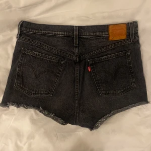 Levi's jeansshorts - Snygga svarta/gråa jeansshorts från Levi's med hög midja. Klassisk femficksmodell med knappar framtill och ikonisk läderpatch bak.👖Säljer dessa då de ej kommer till användning längre. Köpte dessa för ett par år sedan så dem är ganska använda 😇, däremot finns det inga defekter.🙌🏽🤩