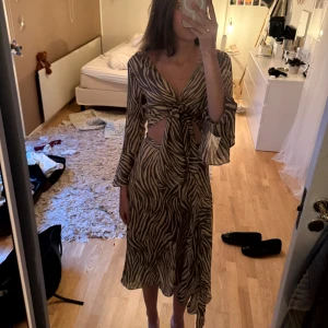Zebramönstrad långklänning från adoore - Säljs inte längre! Säljer en snygg långklänning med zebramönster i beige och brunt. Klänningen har v-ringning, knyt framtill, cut-outs vid midjan och vida ärmar. Från adoore, säljer pga tyvärr för liten för mig! Använd bara 2 ggr! 