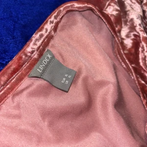 Rosa sammetsklänning från Lindex XL - Supersnygg kort klänning i rosa krossad sammet från Lindex. Den har rund halsringning och korta ärmar, perfekt för dig som vill sticka ut med en glansig och mjuk look. Passar dig som gillar trendiga material och vill ha något bekvämt men ändå extra.