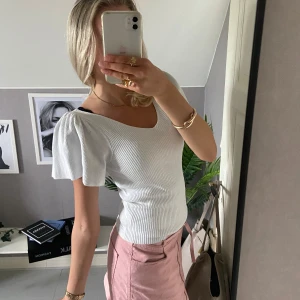 Vit ribbad topp med puffärm från ONLY - Superfin vit ribbad topp från ONLY med korta puffärmar och v-ringning både fram och bak. Snygg knytning i ryggen som ger en extra detalj. Stretchigt material som sitter snyggt och bekvämt. Perfekt till jeans eller kjol för en fräsch look.