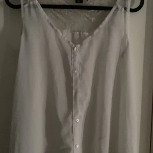 Vit linnetopp med knappar - Säljer en stilren vit linnetopp med v-ringning och knappar framtill. Toppen är ärmlös och har en enkel, clean design som passar perfekt till jeans eller kjol. Lätt och luftig för varma dagar.