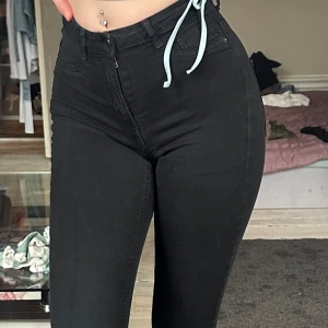 Svarta skinny jeans med hög midja - Säljer ett par svarta skinny jeans med hög midja och klassiska bakfickor. Jeansen har en tight passform och är tillverkade i stretchigt denimtyg som sitter snyggt på kroppen. 