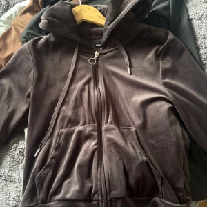 Brun velour kofta från Gina Tricot - Mysig brun kofta i mjuk velour från Gina Tricot. Koftan har huva med snörning, dragkedja framtill med ringdetalj och stora fickor. Perfekt för chill dagar och snygg att styla med jeans eller mjukisbyxor.