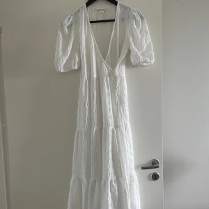 Vit långklänning med puffärm - Superfin vit långklänning från Monki med v-ringning och puffiga korta ärmar. Klänningen har omlottkänsla framtill och är sydd i ett lätt strukturerat tyg av polyester med lite stretch. Perfekt för sommarens alla tillfällen.