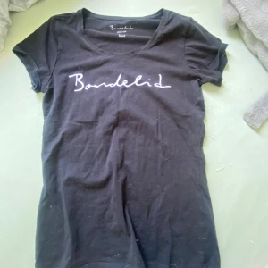 Svart t-shirt från Bondelid - Svart t-shirt från Bondelid med vit logga tryckt framtill. Använd endast 1 gång, så typ som ny. Klassisk rund halsringning och korta ärmar. T-shirten är i mjuk bomull och har en enkel, stilren design som passar perfekt till jeans eller shorts.