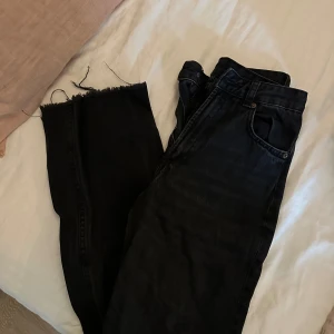 Svarta jeans från Zara med rå kant, hög midja full längd  - Svarta jeans från Zara i klassisk femficksmodell. Jeansen har hög midja och raka ben med rå, avklippt kant nertill för en edgy vibe. Tillverkade i jeansmaterial med en mörk tvätt. Perfekta för dig som gillar en trendig och avslappnad look.