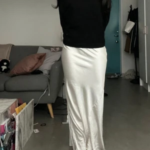 Vit satinkjol  - Säljer en lång, vit satinkjol. Kjolen har en glansig finish och sitter figurnära över höfterna innan den faller rakt ner. Perfekt för dig som gillar en clean och elegant look.