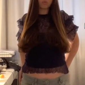 Mörklblå spetsblus med volangärmar - Supersnygg svart blus i transparent spets med volangdetaljer på ärmarna. Kortärmad modell med rund hals. Perfekt att styla med jeans eller kjol för en trendig look.