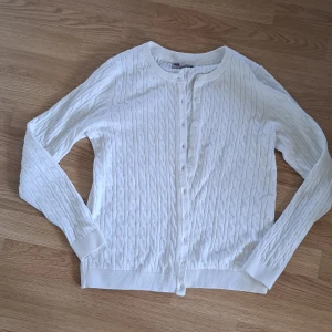 Vit kabelstickad kofta Basic You - Vit kabelstickad kofta från Basic You i ekologisk bomull. Klassisk rund halsringning, långa ärmar och knäppning framtill med små vita knappar. Snygg ribbad kant vid ärmslut och nederkant. Perfekt för lager-på-lager och enkel att matcha.💕