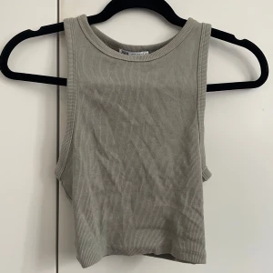 Ribbad grönt linnetopp från Zara - Snygg ribbad linnetopp från Zara i en neutral grön färg. Modellen är ärmlös med rund halsringning och croppad passform, perfekt till jeans eller kjol. Enkel och stilren design som funkar till många olika looks.