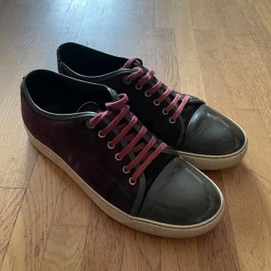Vinröda sneakers med lackad tå - Snygga lanvins i vinröd mocka med svarta lackade tår och matchande vinröda snören. Skorna är i 6/10 skick. Hör av dig vid minsta fundering👍