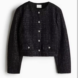 Svart kavajjacka med glittriga knappar - Stilren svart kavajjacka i tweed-look med glittriga knappar framtill. Jackan har rund halsringning, två fickor och lång ärm. Perfekt för dig som vill ha en klassisk men ändå trendig vibe.