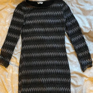 Svart och grå mönstrad klänning - Snygg svart och grå kortklänning från H&M med långärmad design och coolt zigzag-mönster. Klänningen har en figurnära passform och är tillverkad i ett glittrigt material som ger extra edge till looken.