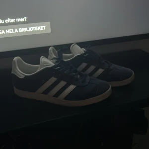Adidas Gazelle sneakers marinblå/vit - Snygga Adidas Gazelle sneakers i marinblå mocka med klassiska vita ränder och vit hälkappa med Adidas-logga. Platt sula och rund tå, perfekt för en clean streetstyle. Skorna har snörning och den ikoniska retrolooken som aldrig går ur tiden. Skriv i Dm över eventuella frågor, pris är självklart diskuterarbat 