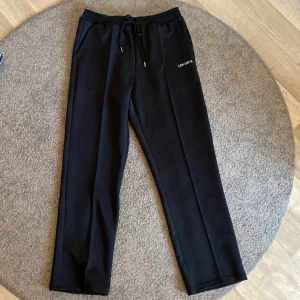 Svarta trackpants från Les Deux - Svarta mjukisbyxor från Les Deux med raka ben och dragsko i midjan. Byxorna har diskret logga på vänster sida och är tillverkade i mjukt material som passar perfekt för en avslappnad stil. Helt oanvända, köpta för 1099!