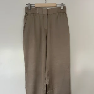 Byxor, Massimo Dutti, 36, beige - Bekväma byxor från Massimo Duttii en lös passform med resår i midjan och bensluten. Byxorna har en dragkedja och knappstängning framtill, samt fickor både fram och bak. Storlek 36. Nyskick. 49% acetate, 48% viskos.    Mått:  Midja ca 36 cm Stuss ca 40 cm Längd yttre ca 87 cm Längd inre ca 60 cm