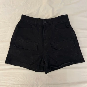 Svarta shorts med fickor från Stay - Svarta shorts från Stay med normal passform och stora fickor framtill. Klassisk design med knapp och dragkedja i midjan. Perfekta för sommaren i strl s