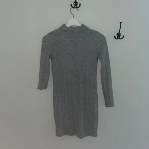 Grå ribbad klänning från SHEIN - En enkel och stilren grå ribbad klänning från SHEIN med trekvartsärm och rak passform. En arm vart inte helt nervikt men dom ska vara lika långa😅Perfekt för dig som gillar en minimalistisk look. Klänningen har en hög hals och är tillverkad i ett mjukt, stretchigt material. Använde alltid den när jag var yngre men för liten för mig nu.