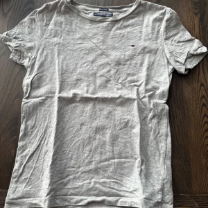 Ljusgrå t-shirt från Tommy Hilfiger - Snygg ljusgrå t-shirt från Tommy Hilfiger i mjuk bomull. Lite skrynklig eftersom att den legat i garderoben ett tag. Fint skick. Skriv till mig om ni har några frågor!