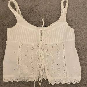 Vit broderad topp med knytning - Säljer en jätte söt vit topp med broderade blommor, spetsdetaljer och knytning där fram. Helt perfekt topp nu till sommaren.