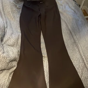 Bruna kostymbyxor från Gina Tricot - Säljer ett par svarta kostymbyxor från Gina Tricot i storlek M. Byxorna har en klassisk passform med utsvängda ben och hög midja. Perfekta att styla med en snygg topp eller skjorta. Använda ett fåtal gånger.