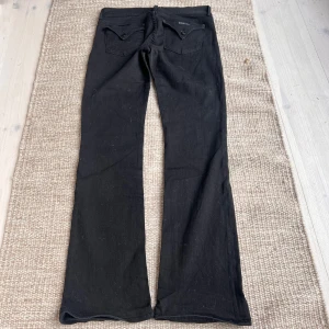Svarta bootcut jeans  - Svarta jeans från HUDSON USA med bootcut passform. Klassisk femficksdesign, knappgylf och diskret röd detalj vid fickan. Snygga och stilrena jeans som passar till många olika looks.