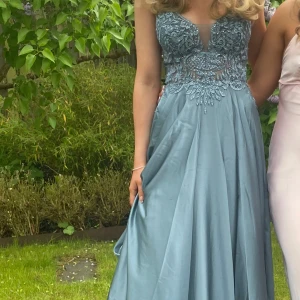 Ljusblå balklänning  med spetsdetaljer  - Elegant ljusblå balklänning med v-ringad överdel och vackra spetsdetaljer. Klänningen har ärmlös design och markerad midja, vilket ger en klassisk och stilren siluett. Perfekt för bal eller festliga tillfällen.  Slutsåld på zalando användes vid ett tillfälle.