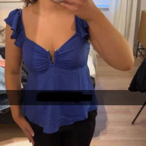 Blå topp med v-ringning - Säljer en blå topp med volangdetaljer vid axlarna och v-ringning. Toppen har en figurnära passform upptill och faller ut nertill. Köpt på vero Moda men märket är aware 💕