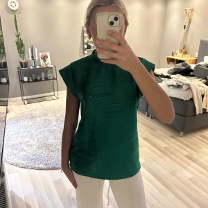 Grön topp med strukturmönster - Säljer en grön topp med coolt strukturmönster och korta ärmar. Toppen har en rund halsringning och en liten knappöppning bak i nacken. Perfekt för dig som vill ha något enkelt men ändå speciellt.