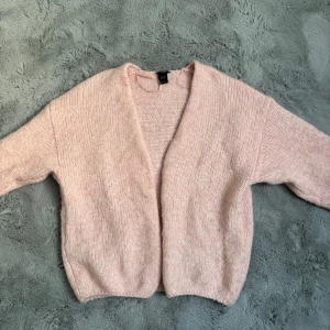 Ljusrosa stickad kofta från Lindex - Mysig ljusrosa stickad kofta från Lindex. Koftan är öppen framtill utan knappar och har långa ärmar. Perfekt att slänga på sig över en topp för en avslappnad look.
