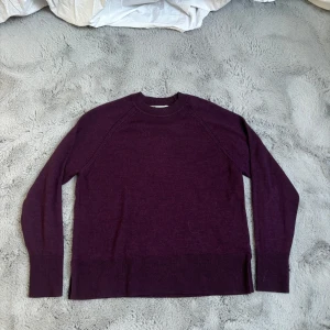 Mörklila stickad tröja - En enkel och stilren mörklila stickad tröja med rund halsringning och långa ärmar. Tröjan har ribbade muddar vid ärmslut och nederkant, perfekt för lager-på-lager under kyliga dagar. 
