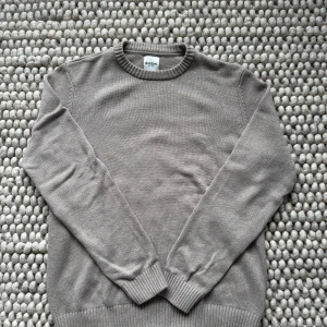 Beige stickad tröja från Dobber - Säljer en stilren beige stickad tröja från Dobber med rund halsringning. Tröjan har långa ärmar och ribbade muddar vid ärmslut och nederkant. Perfekt för lager-på-lager och passar till många olika outfits.