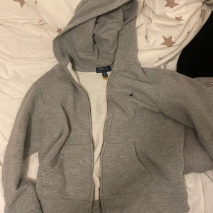 Hej jag säljer en ralph Lauren tröja med dragkedja, jag använder inte den längre jag växt om den men om ni är intresserade så skriv gärna tack 🤩  - Säljer en klassisk grå hoodie från Polo Ralph Lauren med dragkedja och huva. Jackan har två fickor framtill och en liten broderad logga på bröstet. Perfekt för en avslappnad stil.