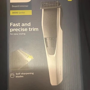 Philips skäggtrimmer 3000 Series - Philips skäggtrimmer från 3000 Series med självslipande blad och justerbar längdinställning. Trimmern har svart och silver design med greppvänligt handtag och tydlig längdskala. Perfekt för att styla och trimma skägget med precision.