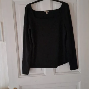 Svart långärmad topp med fyrkantig ringning - En stilren svart långärmad topp med fyrkantig ringning. Perfekt att matcha med jeans eller kjol för en clean look. Tunn och mjuk i materialet, passar dig som gillar minimalistisk stil.