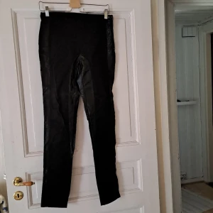 Svarta leggings med glansig finish - Säljer ett par svarta leggings med glansig finish. De har en tight passform och hög midja, perfekta att styla till olika outfits. Materialet känns syntetiskt och ger en cool look.