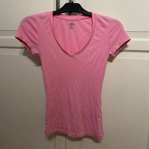 Rosa v-ringad t-shirt från L.O.G.G. - Säljer en enkel och stilren rosa figur sydd t-shirt från L.O.G.G. i storlek XS. T-shirten har v-ringning och korta ärmar, perfekt för en avslappnad look. Tillverkad i mjuk bomull och är stretchig.