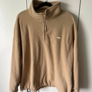 Beige fleece-tröja med halv dragkedja - Mysig beige fleece-tröja från Dazy med hög krage och halv dragkedja framtill. Tröjan har långa ärmar och justerbar dragsko nertill för en skön passform. 