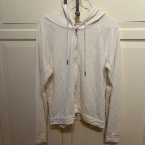 Vit hoodie med dragkedja från H&M - Säljer en enkel och stilren vit zip up hoodie från H&M i storlek S. Tröjan har dragkedja framtill, huva med dragsko och långa ärmar. 
